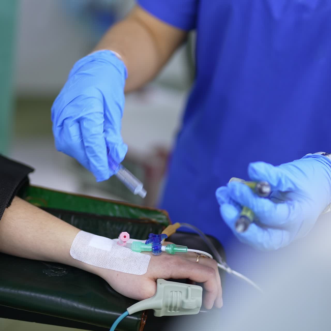 Nurse's gloved hands insert medicines into the tube system connected to patient's hand. Medic uses two syringes to input medications
