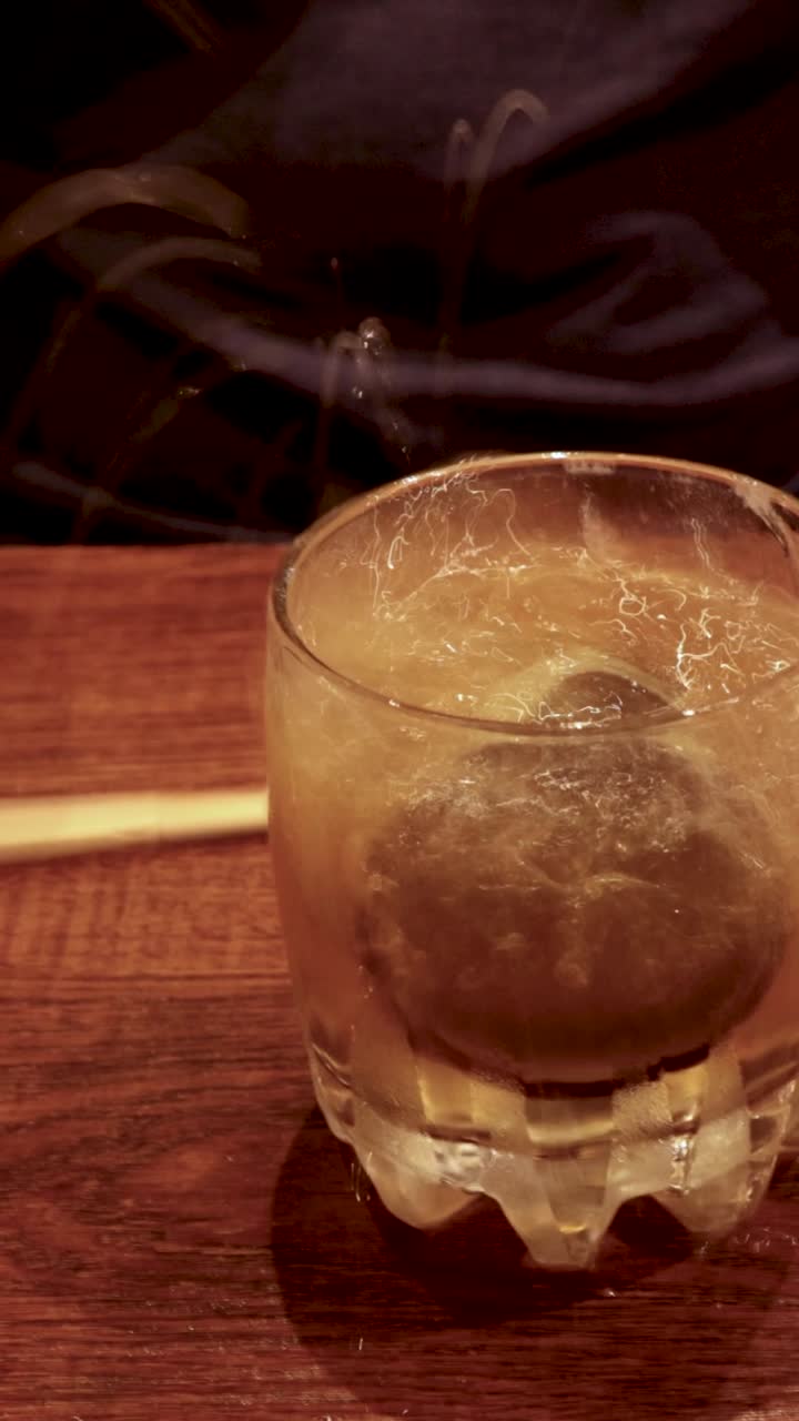 Una tazza da sake cade dalle bacchette in un bicchiere di birra, creando uno schizzo e della schiuma
