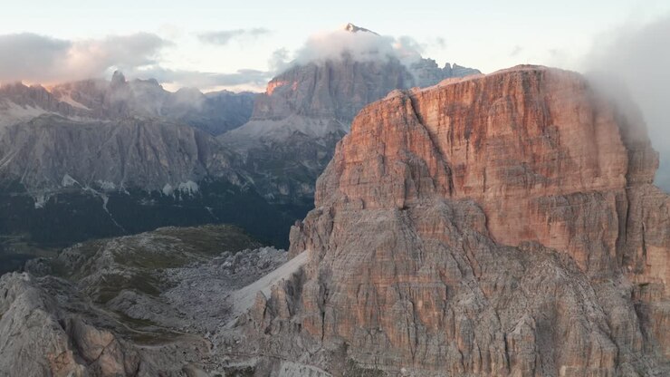 Volo aereo in avanti sopra le montagne illuminate del Gruppo del Nuvolau nelle Dolomiti durante un tramonto dorato