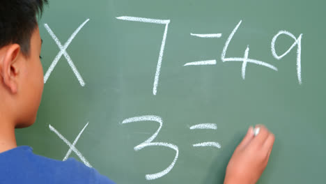 vista trasera de un escolar asiático resolviendo un problema de matemáticas en la pizarra en el aula de la escuela 4k