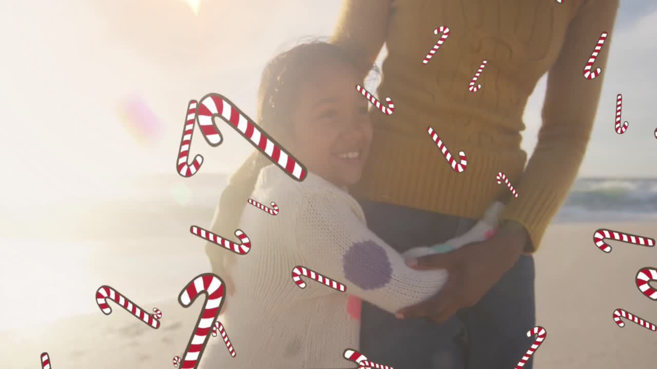 animación de bastones de caramelo sobre mujer biracial con su hija en la playa