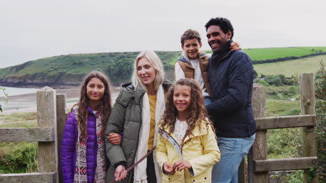 portrait of active multi-cultural family by gate walking along coastal path in fall or winter