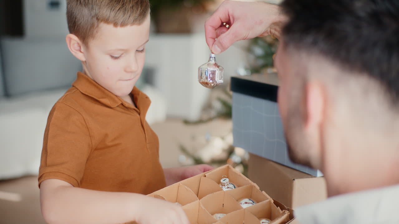 un niño pone bolas de navidad en una caja con su padre.