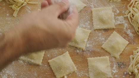 sprinkling flour over ravioli pieces arranges on wooden kitchen table