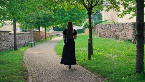 Una-Chica-Con-El-Pelo-Largo-Y-Un-Vestido-Negro-Caminando-Por-Un-Parque-De-La-Ciudad-En-Un-Día-Soleado-De-Verano