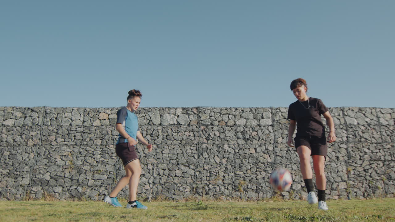 두 명의 스포츠 소녀가 돌 벽에 의해 축구를 하고 있습니다.