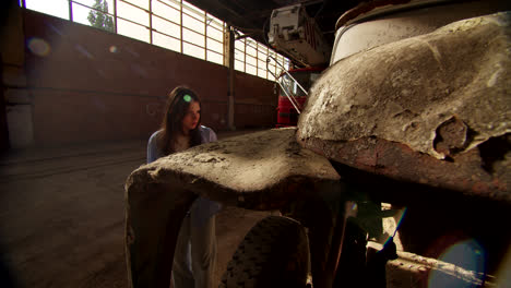 woman looking at a rusty truck in an abandoned warehouse