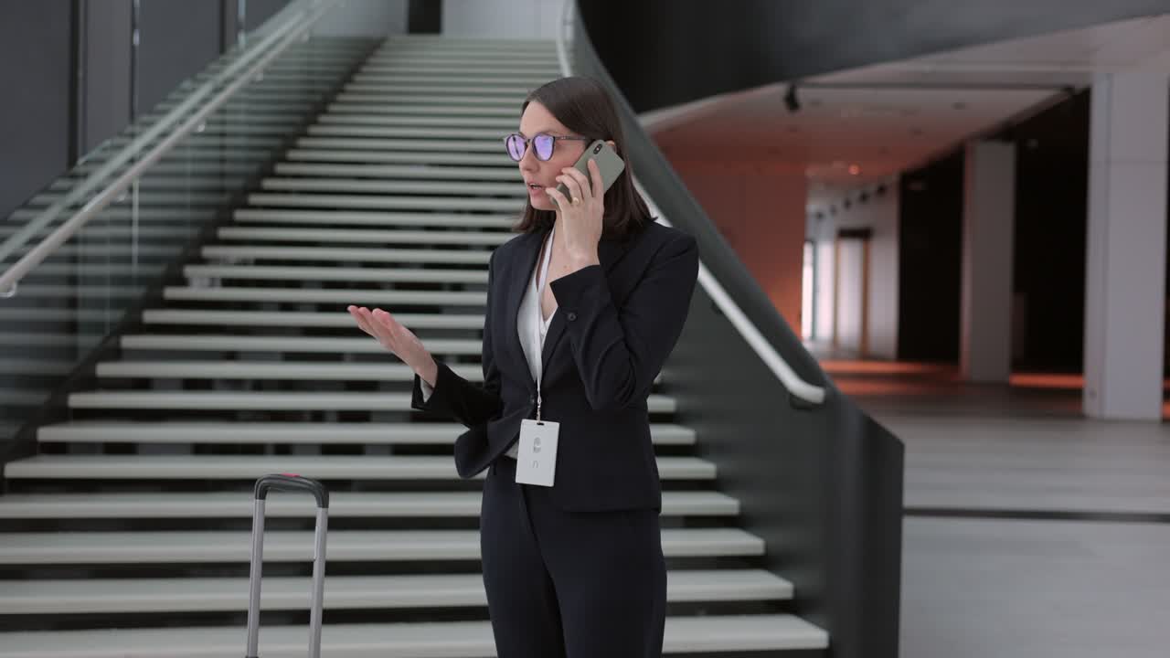 business woman in a business suit with a suitcase walks through the airport or business center and talks on the phone. a European confident woman