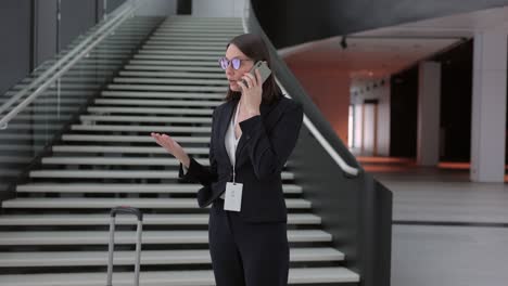 business woman in a business suit with a suitcase walks through the airport or business center and talks on the phone. a european confident woman