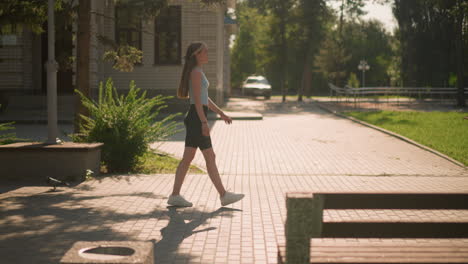 side view of lady walking in slow motion looking focused, wearing casual athletic wear, with a pigeon nearby, background featuring bench, brick building, and blurred view of car near building