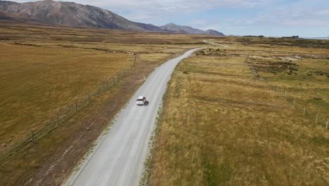 White-SUV-on-dusty-gravel-road-in-rural-countryside-with-mountains-in-background