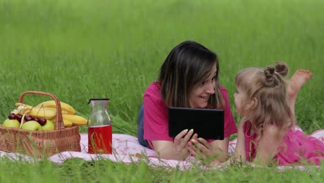 Family-weekend-picnic.-Daughter-child-girl-with-mother-play-online-games-on-tablet.-Chatting