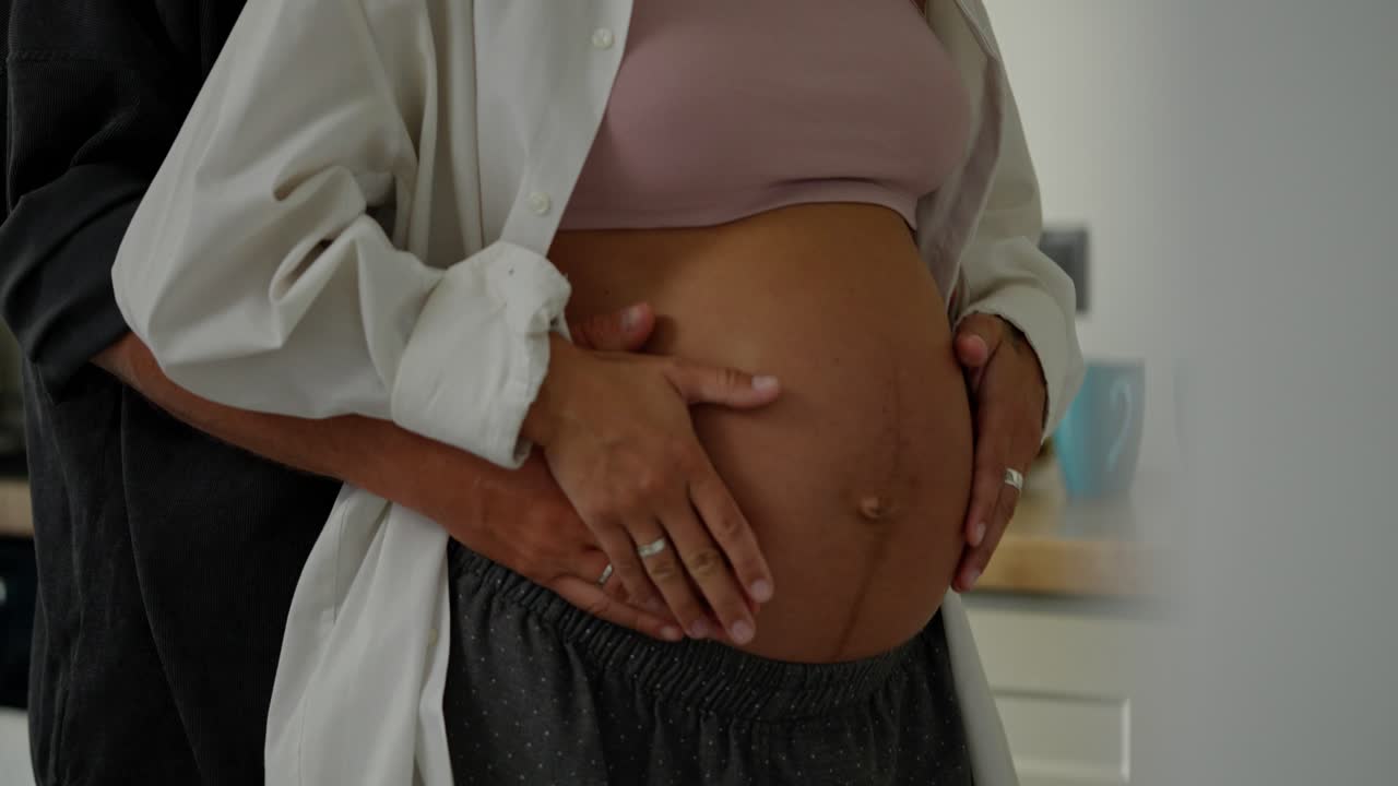 cerca de una feliz mujer embarazada bailando lentamente con su marido en la cocina por la mañana