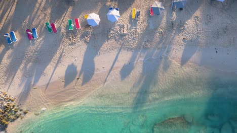 Kristallklare-Meereswellen-Krachen-Sanft-Am-Goldenen-Sandstrand-Mit-Bunten-Stühlen-Und-Sonnenschirmen,-Luftaufnahme-Von-Oben-Nach-Unten