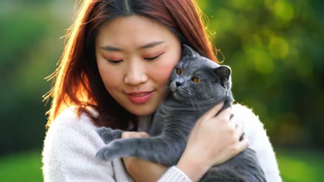 a heartwarming moment of connection: a young woman holds her adorable gray cat close in a sunlit garden, celebrating their unique bond and joyful companionship.