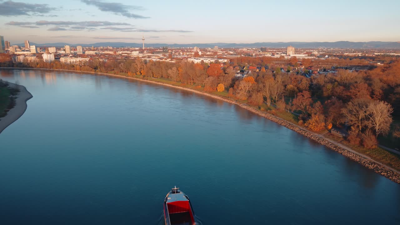 Wide Aerial of Rhine River near Mannheim: Cargo Ship Navigating City Waterfront with Autumn Colors and Sunset Skyline Panorama, Germany