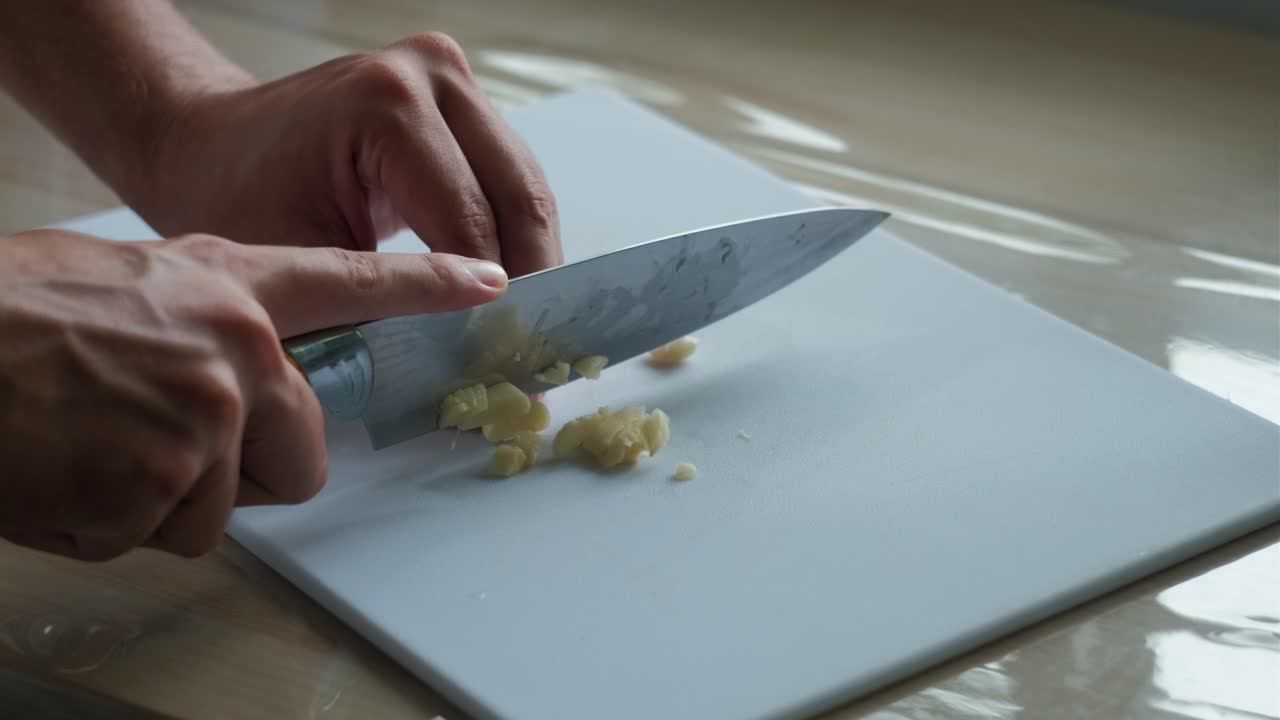 Hands and knife finely chopping garlic on a plastic chopping board. -closeup shot
