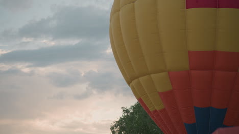 multicolor hot air balloon envelope billowing gently in morning breeze over lush green meadow with distant line of trees under pastel overcast sky sunrise light creating serene slow motion scene