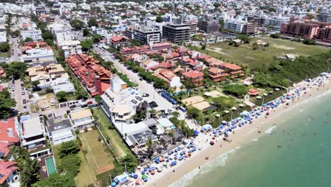 Escena-Aérea-De-Drones-De-Playa-Turística-En-Florianópolis-Con-Muchas-Casas-De-Verano-Hoteles-Frente-Al-Mar-Malla-De-Playa-Urbana-Con-Mucha-Gente-Disfrutando-Del-Sol,-La-Arena-Y-El-Mar