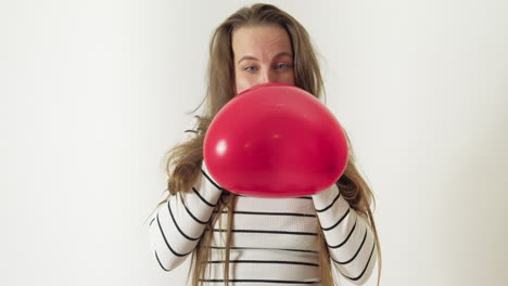 una mujer con el pelo largo infla un globo rojo en forma de corazón con la boca