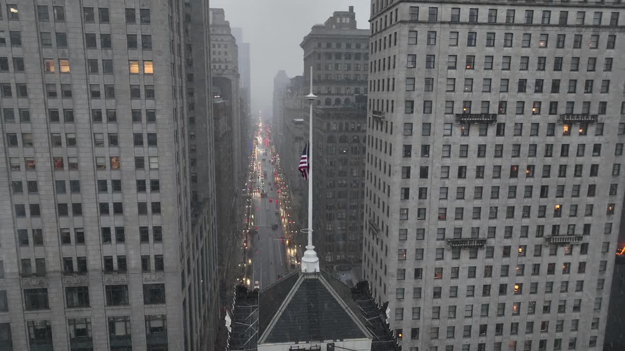 Aerial view of downtown American city street lined with tall buildings, with patriotic United States flag rising above traffic lights in misty winter conditions and urban atmosphere. Philadelphia, PA