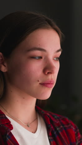 pensive long haired young woman looks out of window standing in room closeup slow motion. lonely lady locked at home during coronavirus lockdown