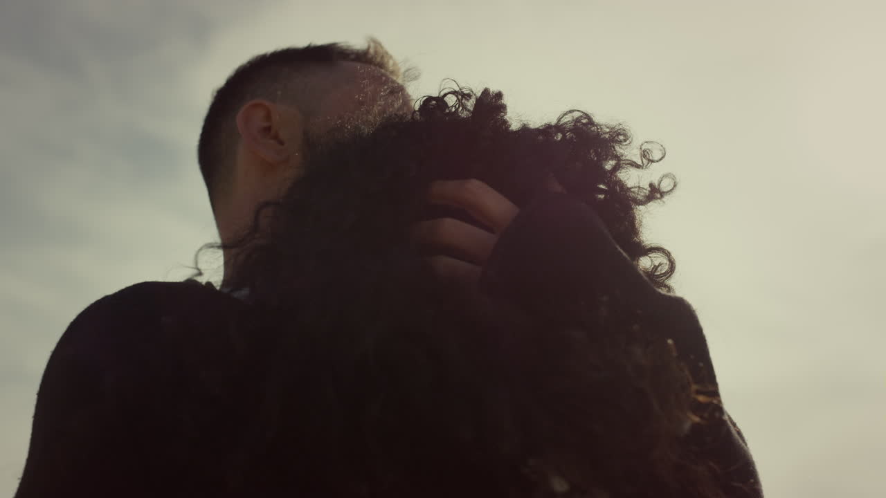 una pareja romántica acurrucada al aire libre, dos amantes tocando el cabello rizado en el cielo al atardecer.