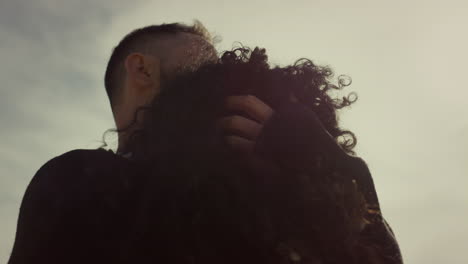 romantic couple cuddling outdoors. two lovers touching curly hair at sunset sky.