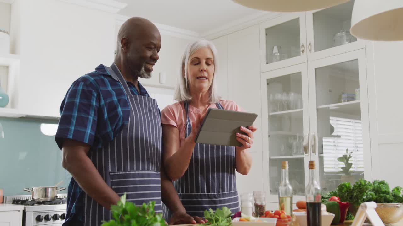 feliz pareja senior diversa usando delantales y cocinando en la cocina
