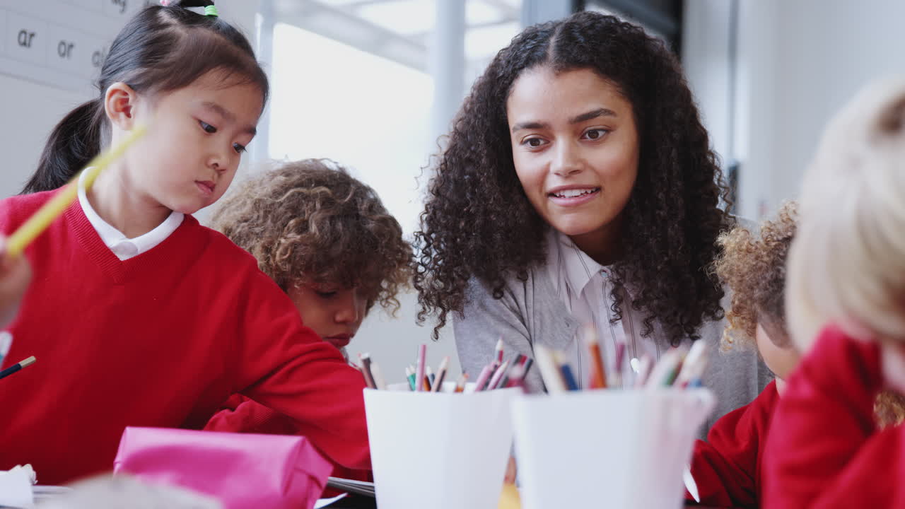 una maestra de escuela infantil sonriente sentada en una mesa en clase con escolares, de cerca