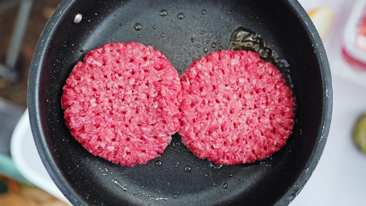 Slow motion frying burgers bubble in oil on outdoor stove in natural light