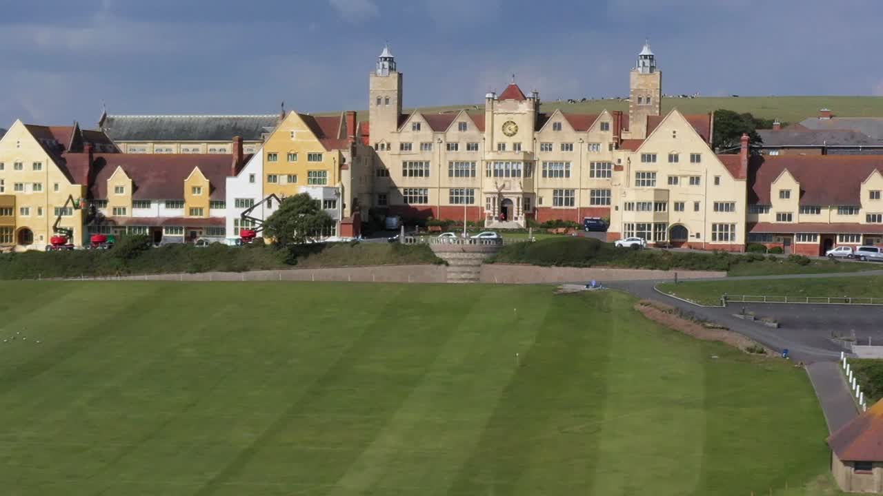 Expansive academic campus with historic architecture, green fields, and parking under a sunny sky