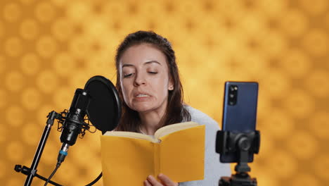 influenciador filmando leyendo un libro con un teléfono inteligente en un trípode, fondo de estudio