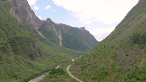 Gudvangen-valley-with-steep-elevated-mountain-slopes-on-bright-sunny-day,-aerial