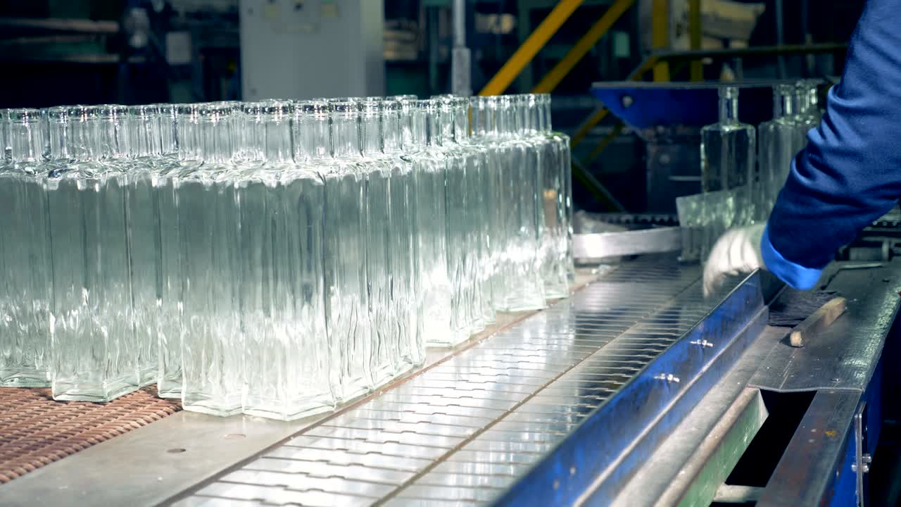 Factory employee is putting glassy bottles onto the conveyor belt