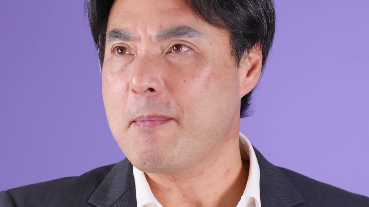 スーツを着たアジア人男性のクローズアップショットで、怒りと不満を表現しています。