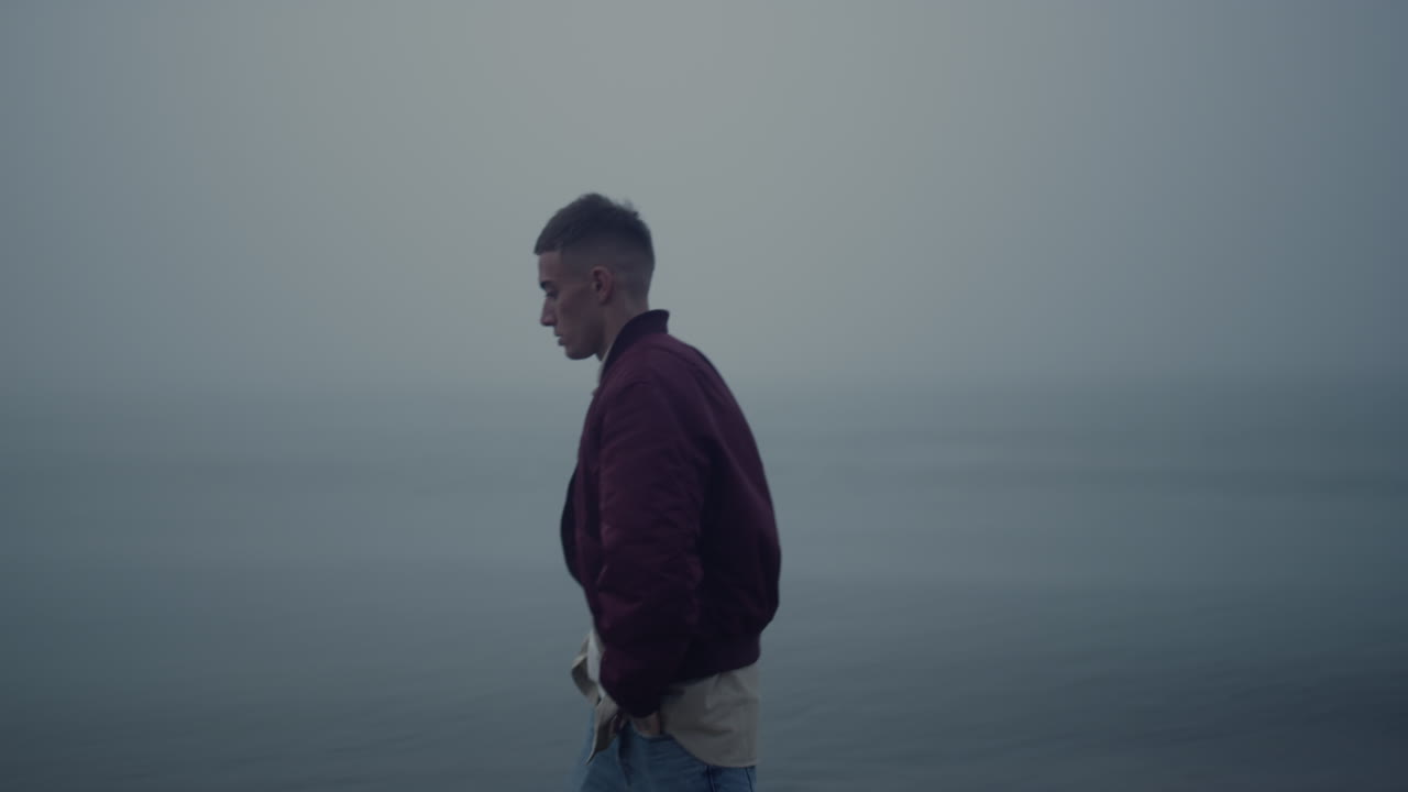 Sad guy walking ocean coast in foggy morning. Casual man looking sea view
