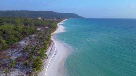 a pristine beach with palm trees meeting the crystal clear turquoise water on koh rong island, cambodia. smooth aerial view flight overflight flyover drone