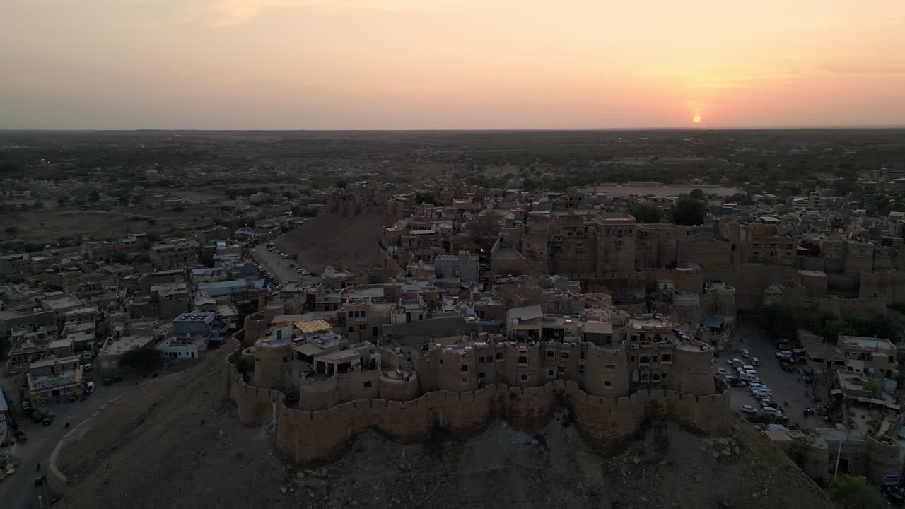 Ripresa orbitale con drone del Forte di Jaisalmer circondato da case di sera con un cielo vibrante, Vista 4K, Rajasthan, India.