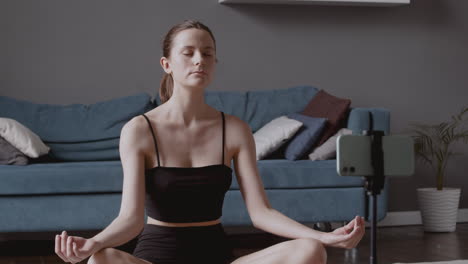 young beautiful woman recording a yoga lesson while in lotus posture and breathing intensely