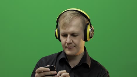 Guy-listens-to-music-in-wireless-yellow-headphones-and-dances.-Green-screen