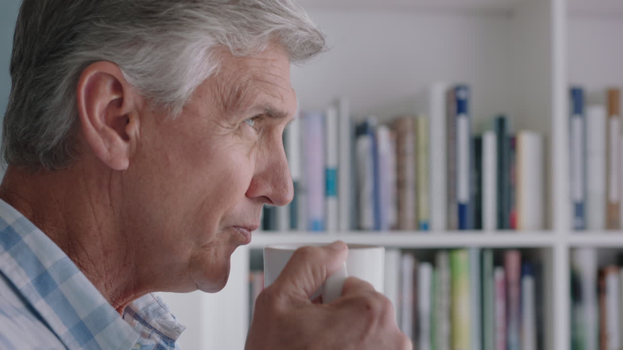 幸せな成熟した男性が自宅でコーヒーを飲み 窓の外を眺め 退職生活を楽しんで 考え深い計画を立てています 4k