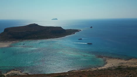 Boats Cruising On Balos Lagoon Near Rocky Island In Chania, Crete, Greece. wide aerial shot