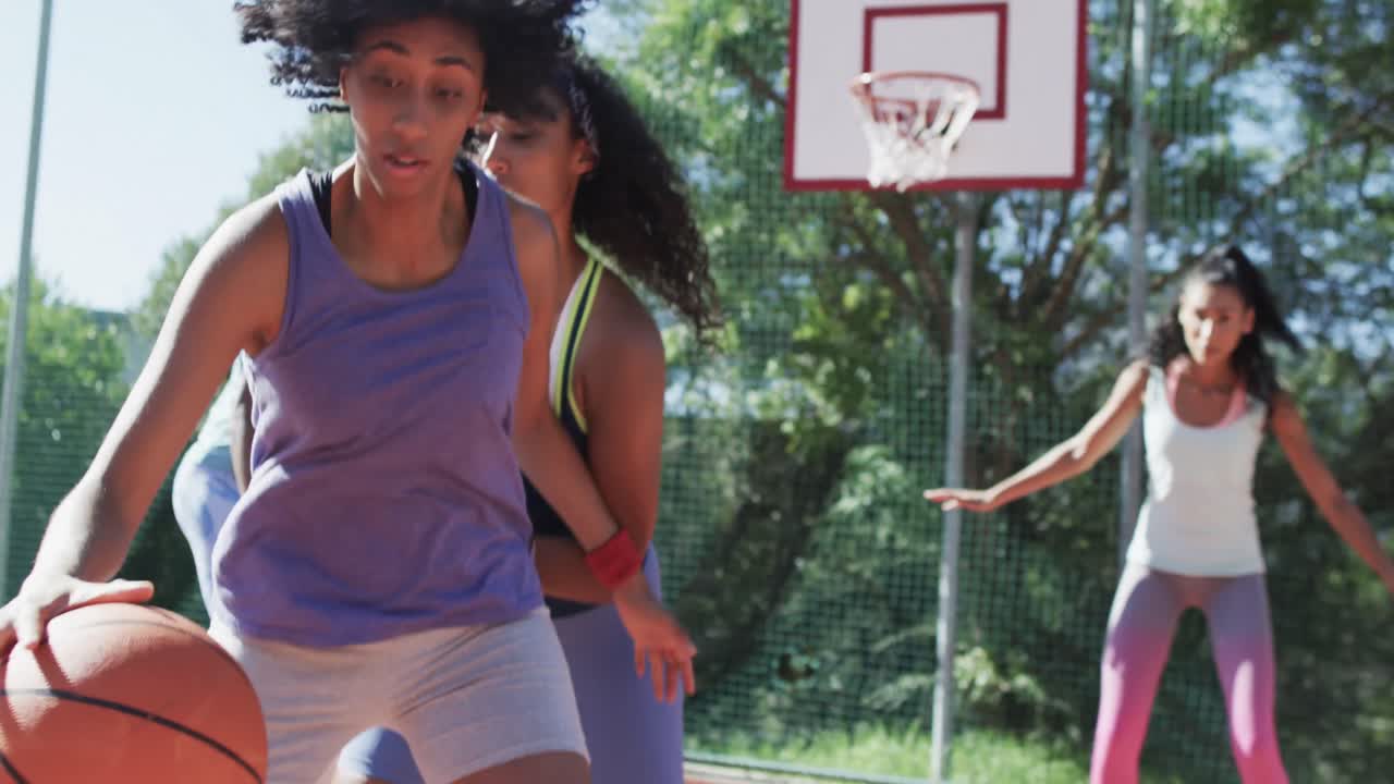 Et glad og mangfoldigt kvindeligt basketballhold træner med mandlig træner på solrig bane, i slowmotion
