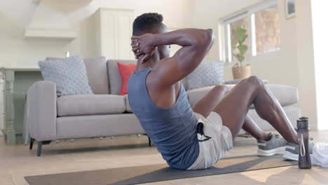 Hombre-Afroamericano-Enfocado-Haciendo-Abdominales-En-Una-Sala-De-Estar-Soleada,-Cámara-Lenta