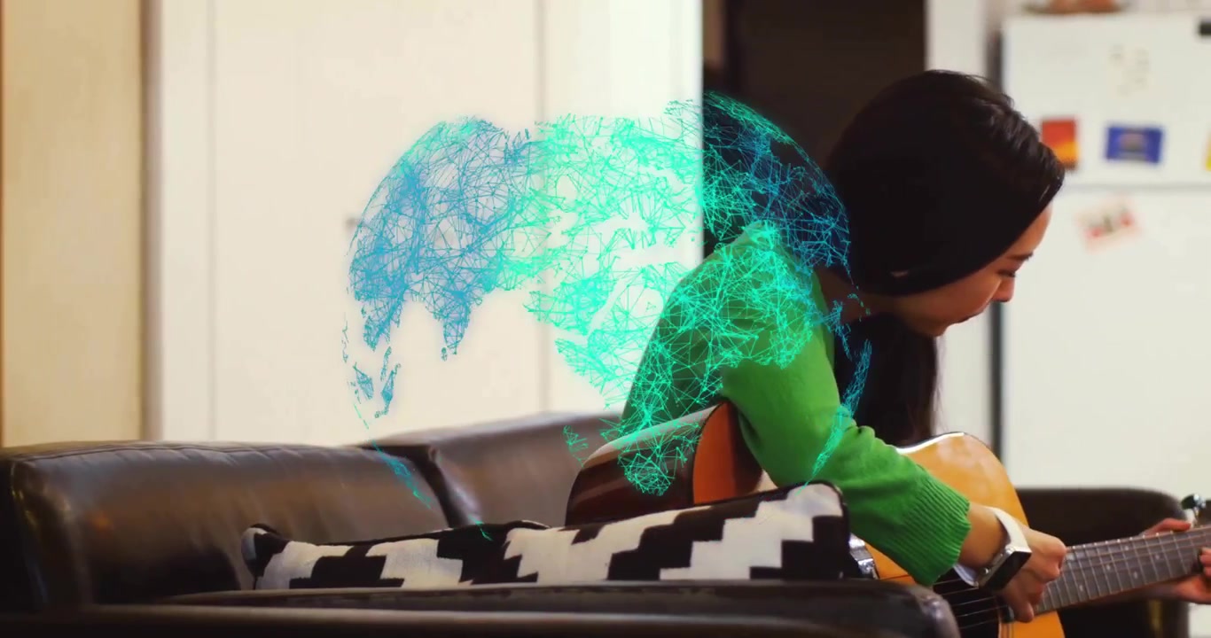 Musician strumming guitar on sofa as tech globe appearing first frame and drifting behind shoulder