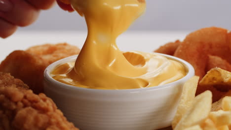 dipping fried chicken and nuggets in cheese sauce