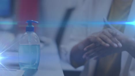 Blue-light-trails-against-mid-section-of-woman-using-hands-sanitizer-at-office