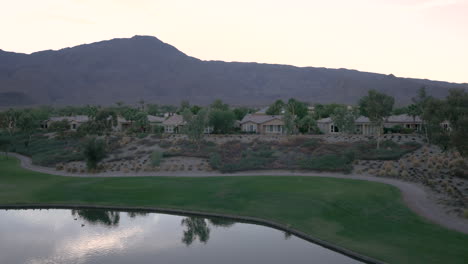 panoramic view of a golf course community with a lake, residential homes, and mountains