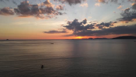 gente remando en una canoa mientras en el fondo un barco tradicional tailandés navega sobre el mar con hermosos colores de puesta de sol
